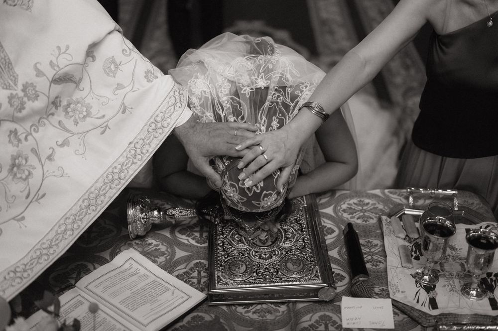 Black and white photo of a Christian baptism ceremony with priest's hands on child's head over a holy Bible.