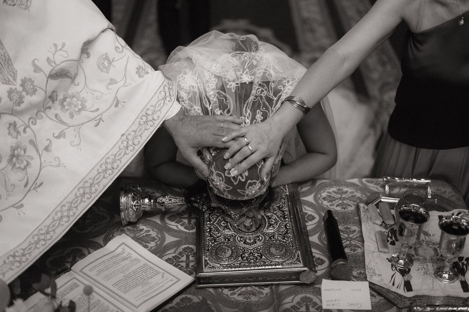 Black and white photo of a Christian baptism ceremony with priest's hands on child's head over a holy Bible.