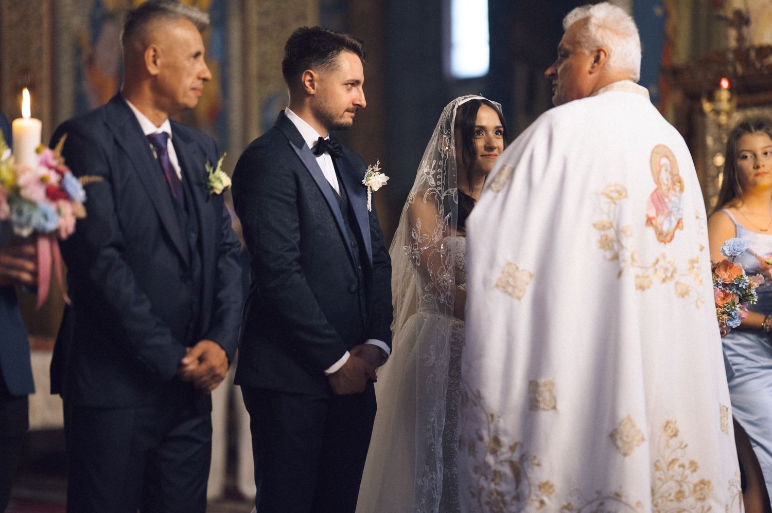 A couple exchanges vows in a traditional church wedding ceremony, officiated by a priest in ornate robes.