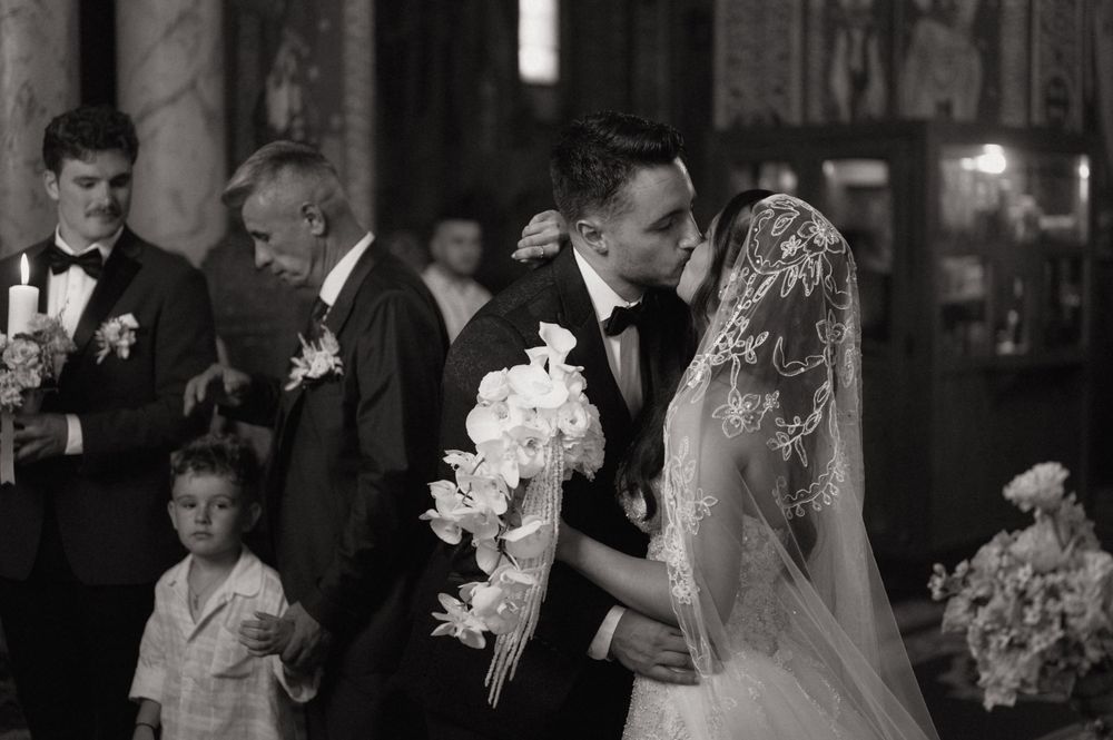 Black and white wedding photo of bride and groom sharing a kiss at the altar during a church ceremony.