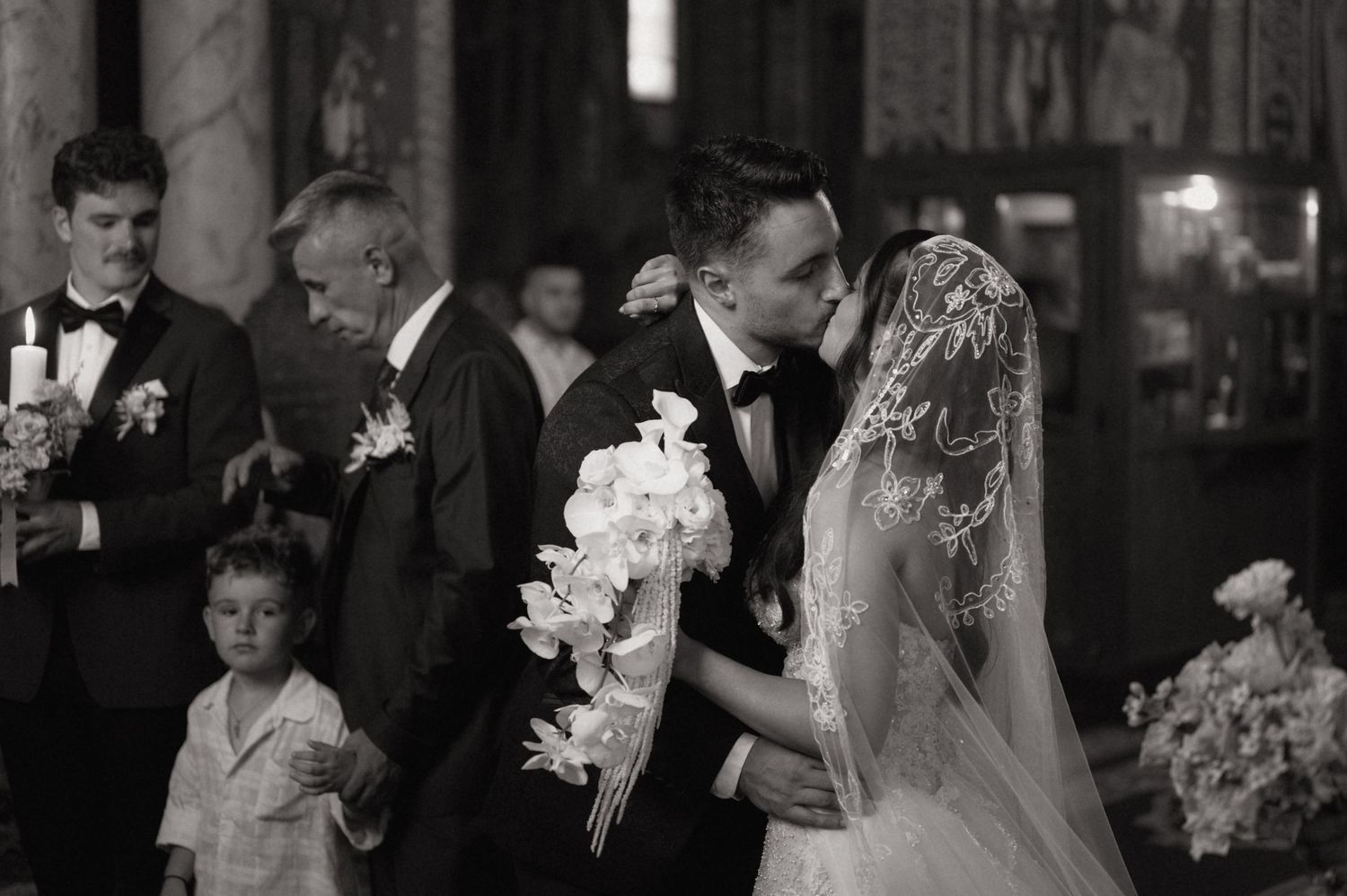 Black and white wedding photo of bride and groom sharing a kiss at the altar during a church ceremony.