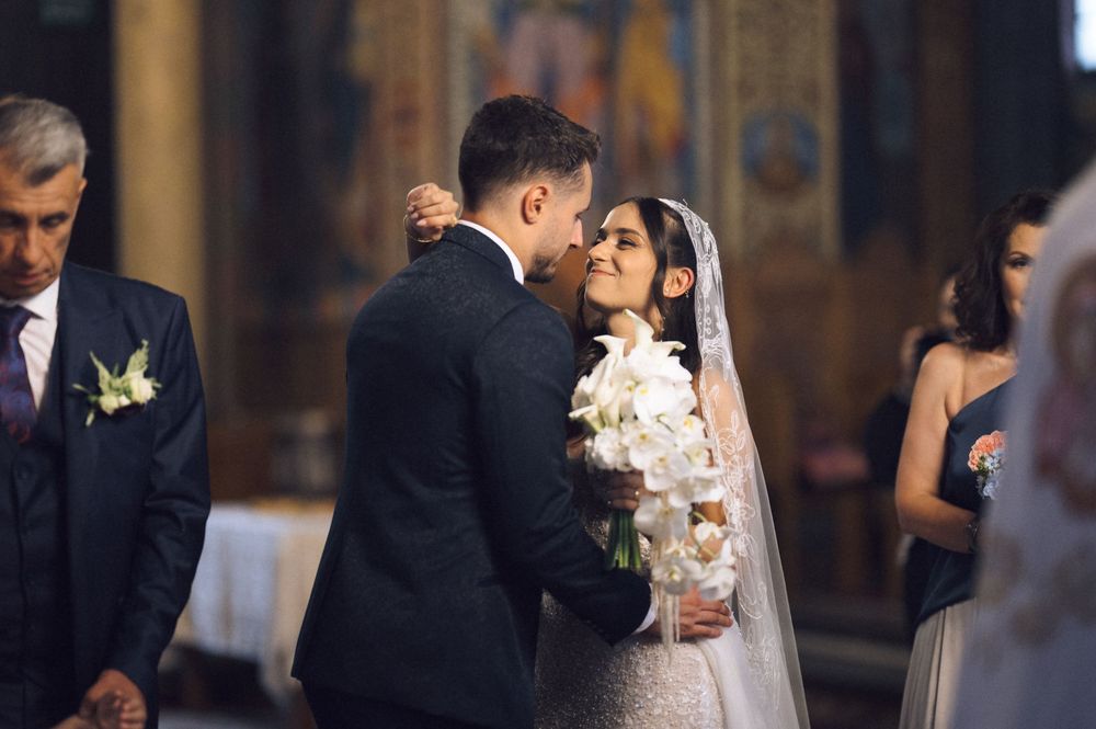 Bride and groom share a tender moment at the altar during a church wedding ceremony, bride holding white orchid bouquet.