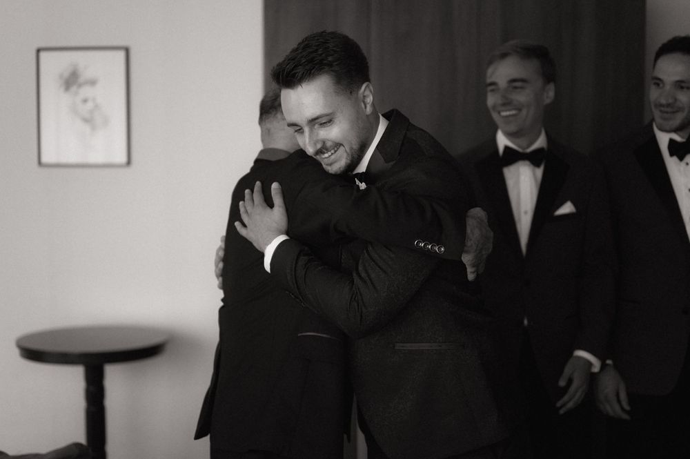 Men in tuxedos sharing a warm hug at a formal event, captured in black and white photography.