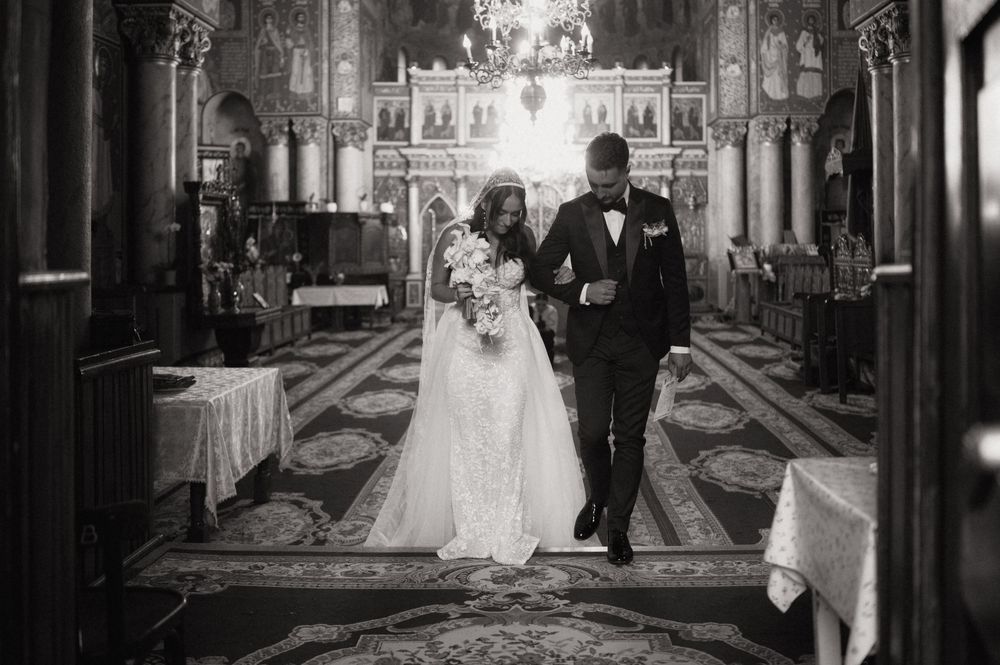 Black and white photo of a bride and groom walking down the aisle of an ornate church on their wedding day.