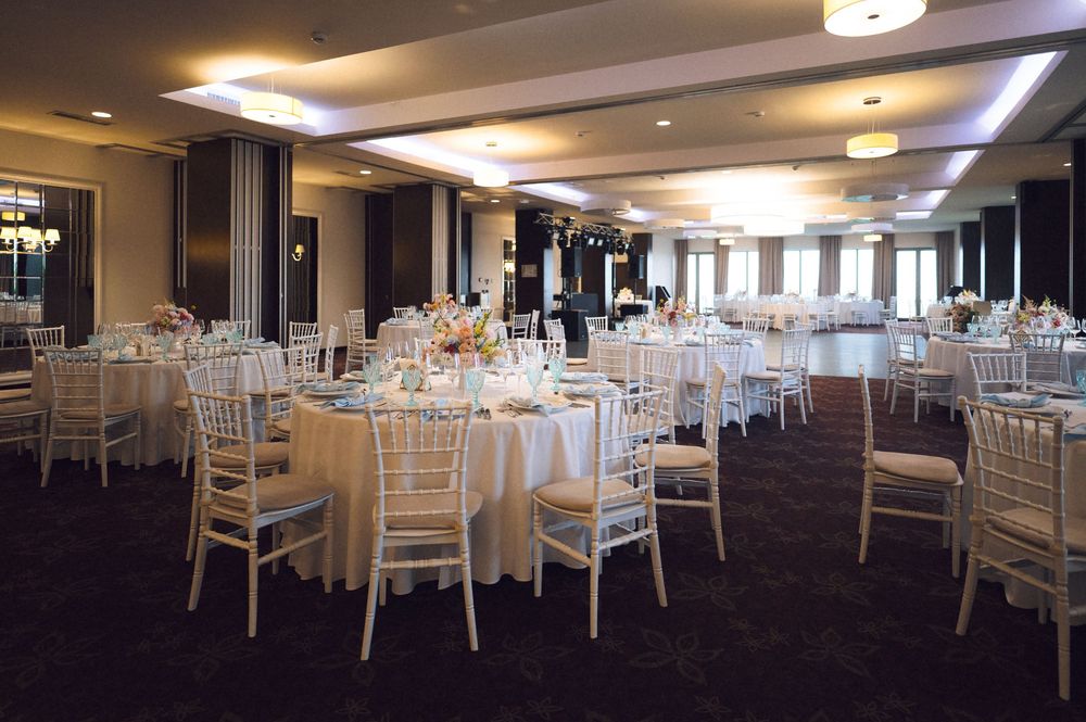 Elegant banquet hall with round tables, white chiavari chairs, floral centerpieces, and soft lighting for a wedding reception.
