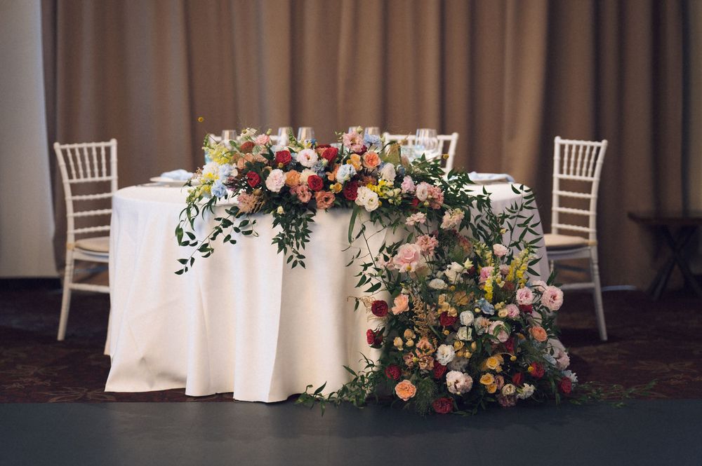 Elegant wedding sweetheart table with white linen and lush floral arrangements featuring roses and greenery.