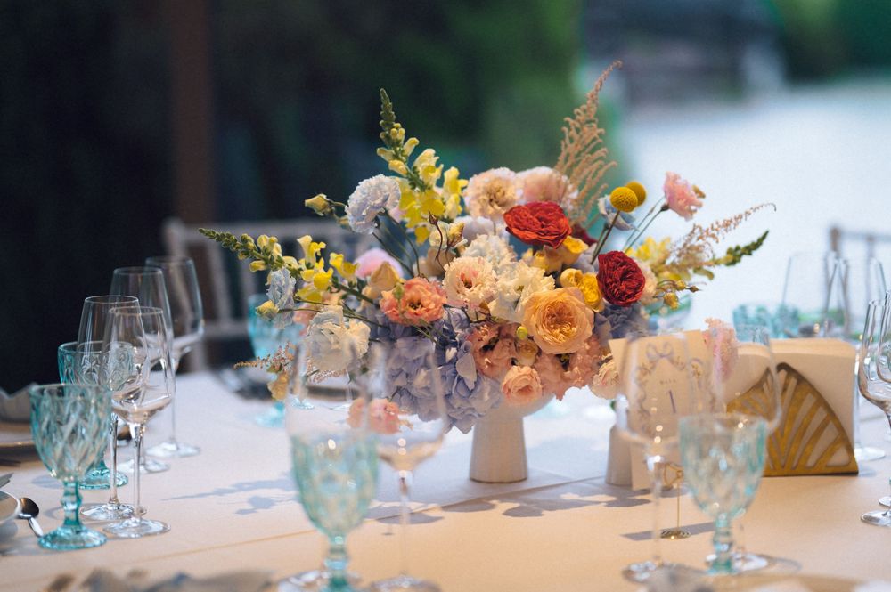 Elegant wedding reception table with colorful floral centerpiece featuring peach, yellow, and red blooms with teal glassware.