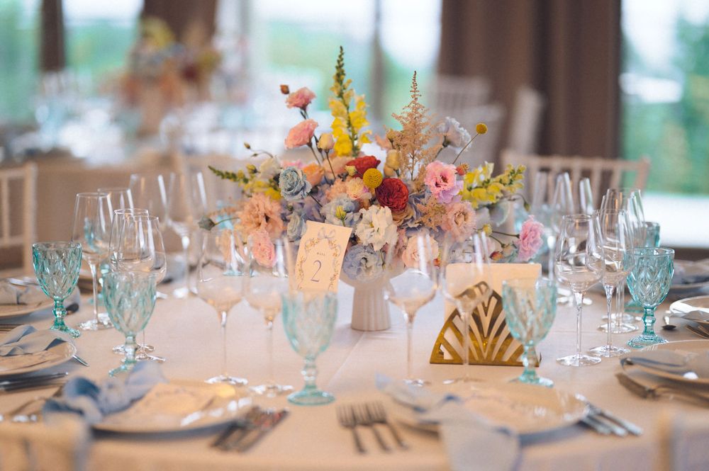 Wedding reception table set with blue glassware, gold accents, and colorful floral centerpiece.