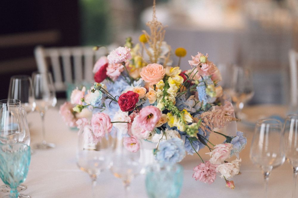Pastel wedding centerpiece with pink, blue, and yellow flowers in a soft floral arrangement on a white reception table.