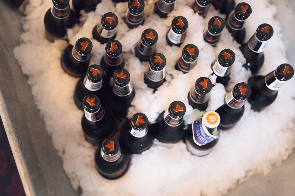 Dark beer bottles chilling on ice in a metal container, perfect for a party or event serving cold drinks.