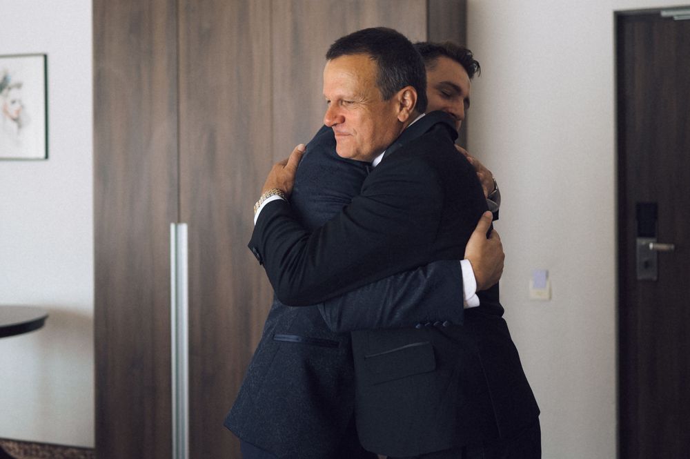 Two men in dark suits share a warm embrace, capturing an emotional moment at a formal event.