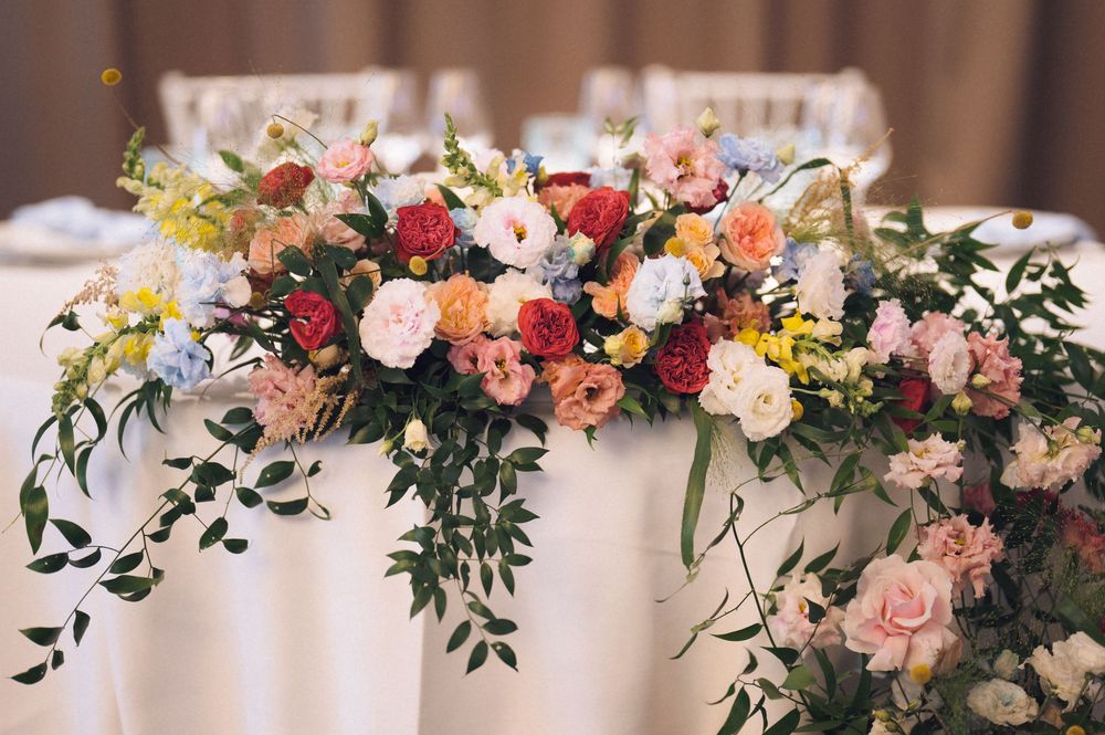 Elegant wedding sweetheart table adorned with lush floral arrangements featuring roses, peonies, and greenery in pink, red, and orange.