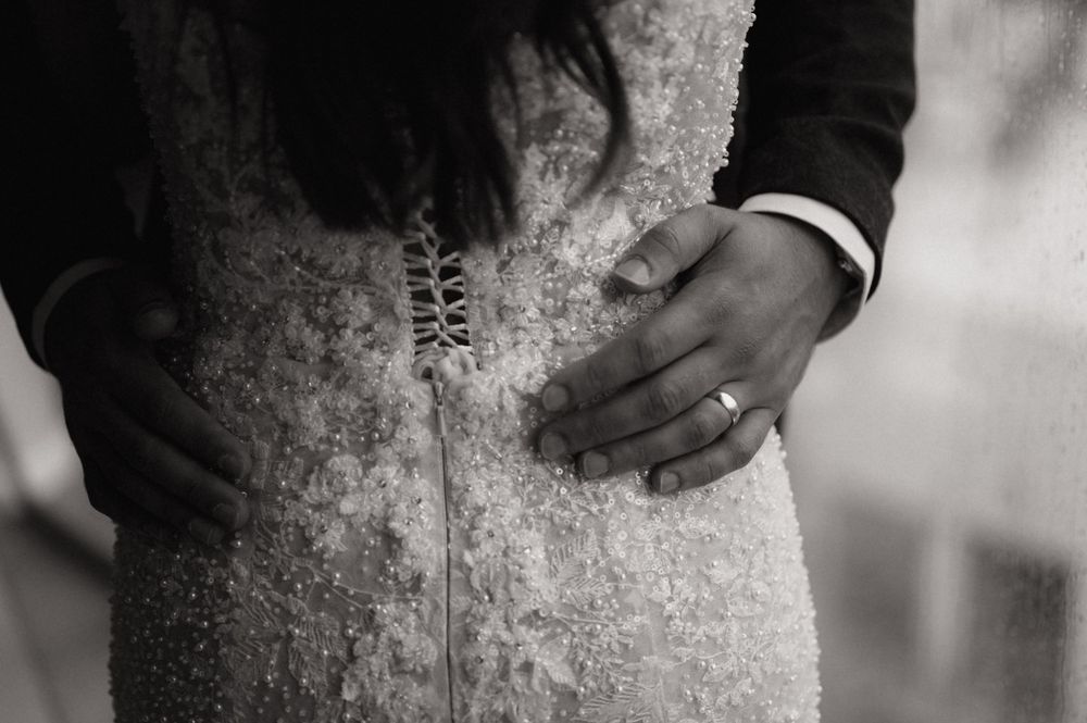 Black and white photo of bride and groom hands on beaded wedding dress with wedding ring visible.