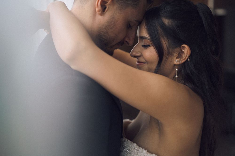 A romantic couple embraces tenderly, the bride in a strapless gown resting her head against her groom in a soft, intimate moment.