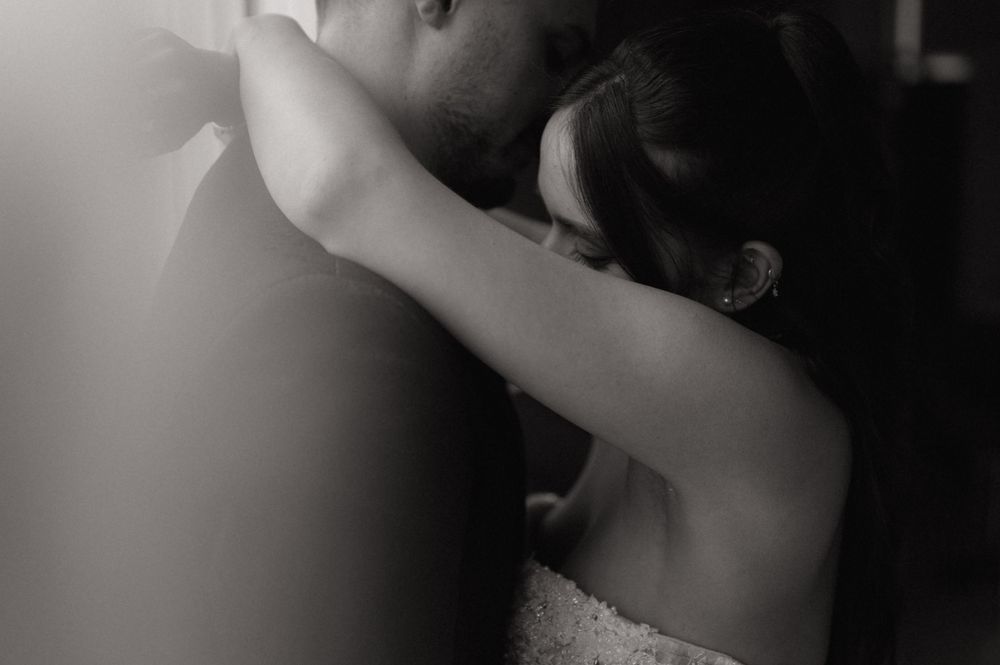 Black and white wedding photo of couple embracing tenderly, bride in lace dress resting head on groom's shoulder.