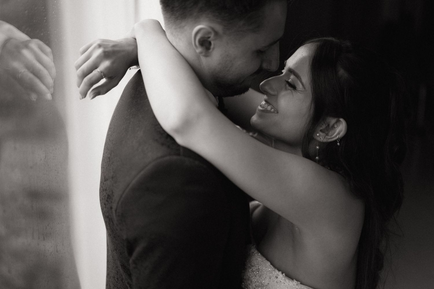 Black and white photo of a smiling bride embracing her groom in a romantic wedding moment.