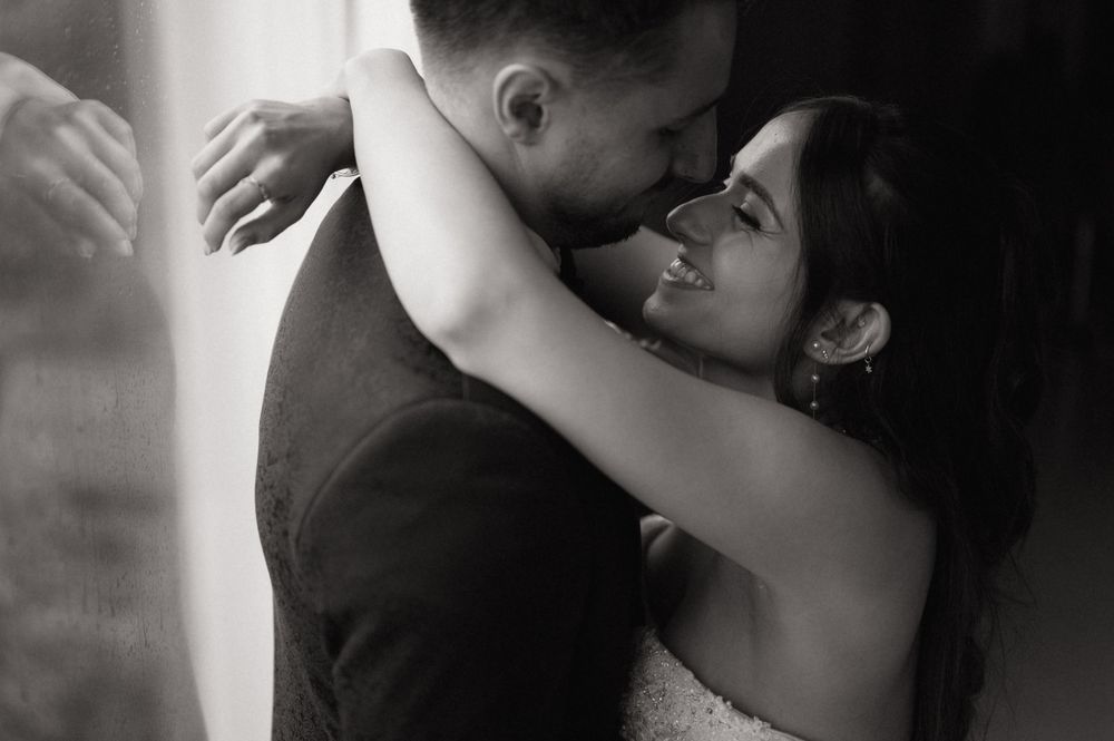 Black and white photo of a smiling bride embracing her groom in a romantic wedding moment.