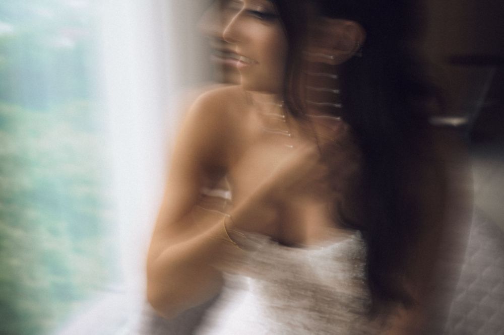 Blurred artistic portrait of a smiling woman wrapped in white towel near a bright window.