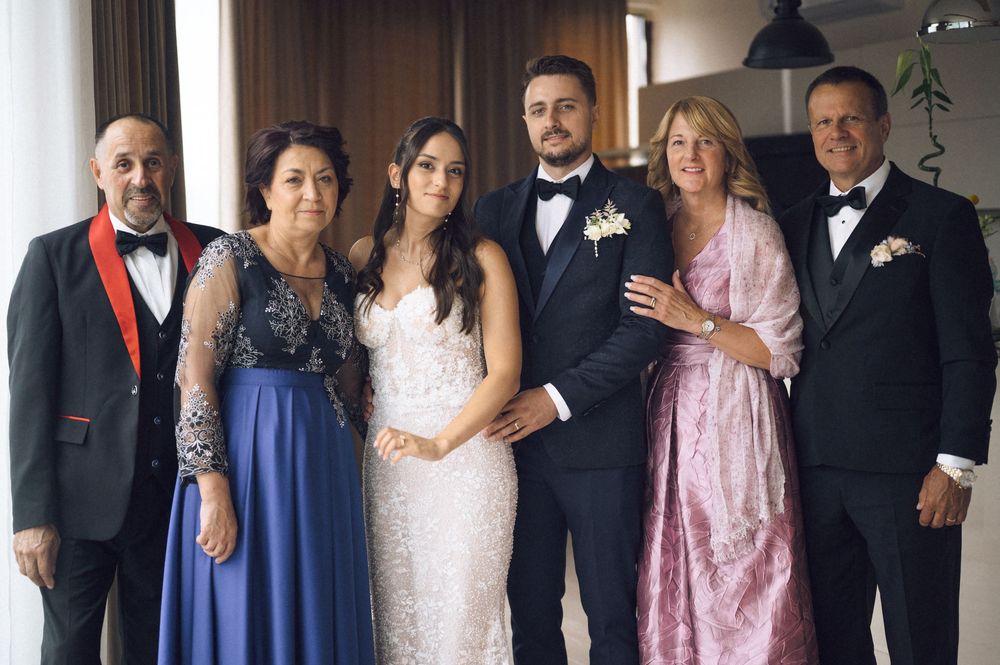 Wedding party of six posing together, bride in white gown, groom in tuxedo, family members in formal attire.