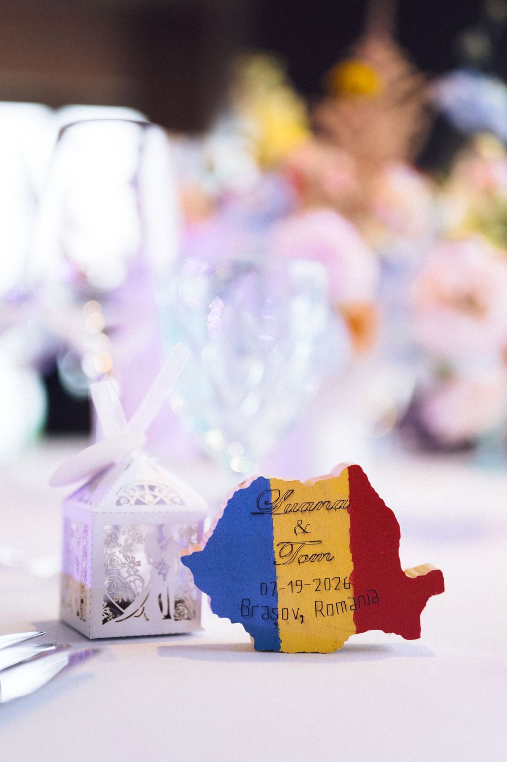 Romanian flag-shaped wedding favor with names and date 07-19-2026, Brasov, Romania on a decorated reception table.