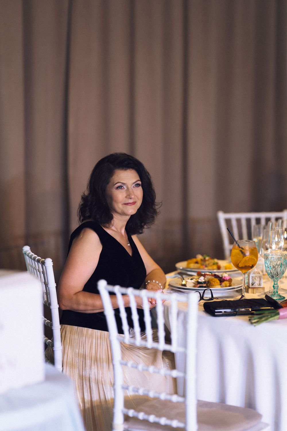 Elegant woman in black dress sitting at a beautifully set banquet table with food and candles at a formal event.