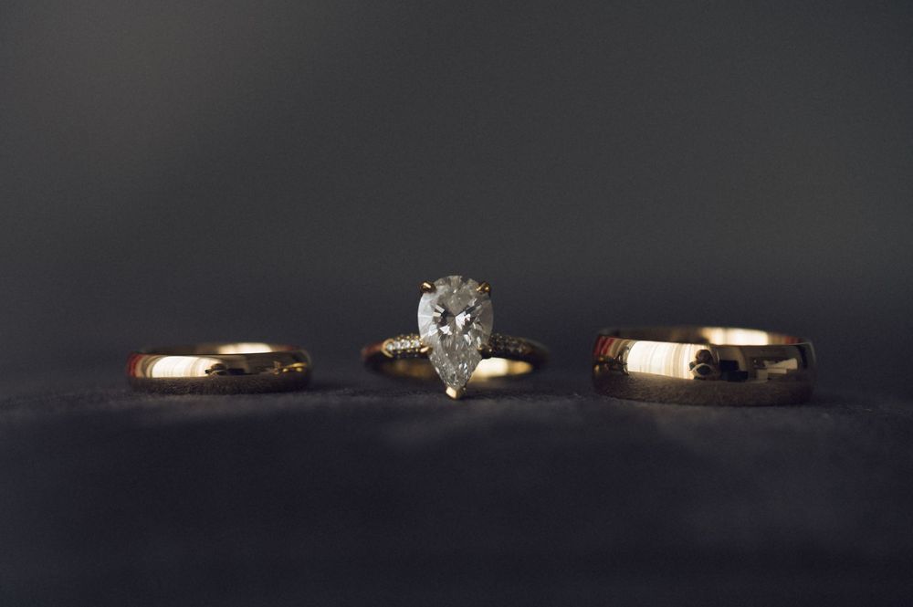 Three gold wedding rings with a pear-shaped diamond engagement ring centered between two plain bands on dark velvet.