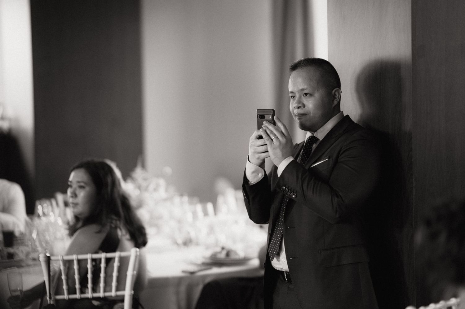 Man in suit photographing with smartphone at elegant wedding reception in black and white.