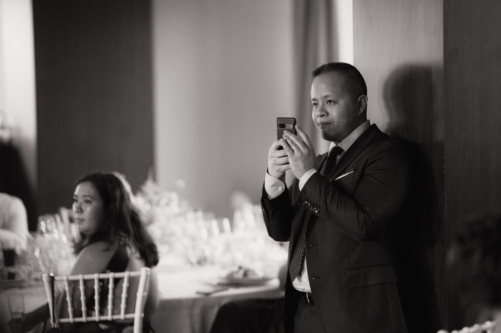 Man in suit photographing with smartphone at elegant wedding reception in black and white.