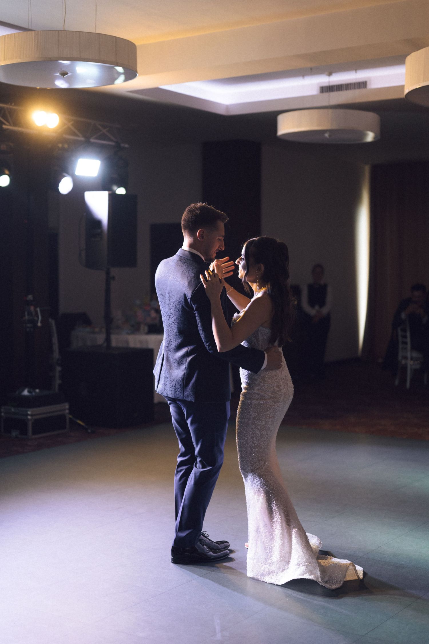 Bride and groom share their first dance in an elegant ballroom, dressed in a suit and fitted white gown.