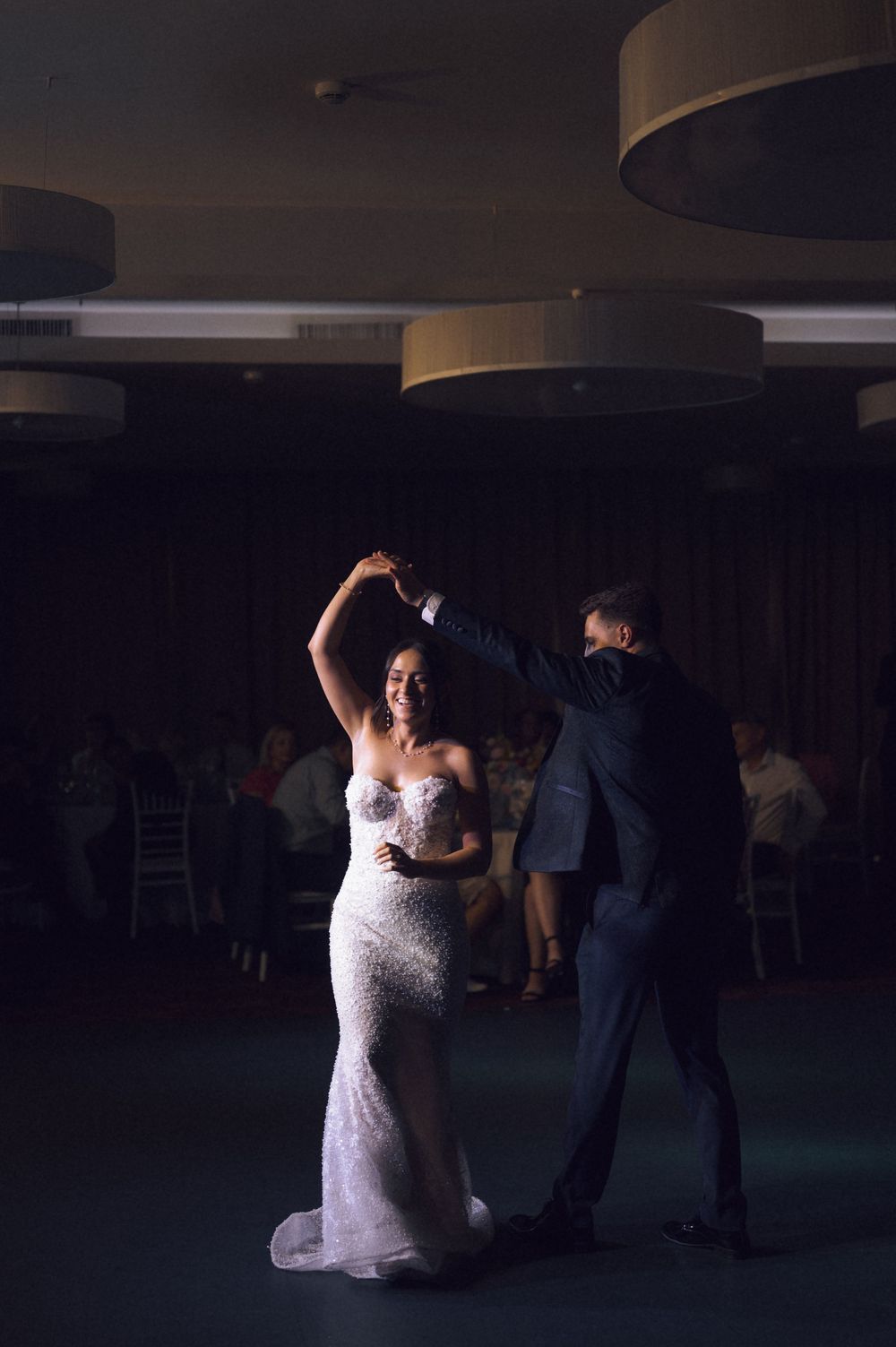 Bride in white gown spins on dance floor with groom in dark suit during elegant wedding reception.