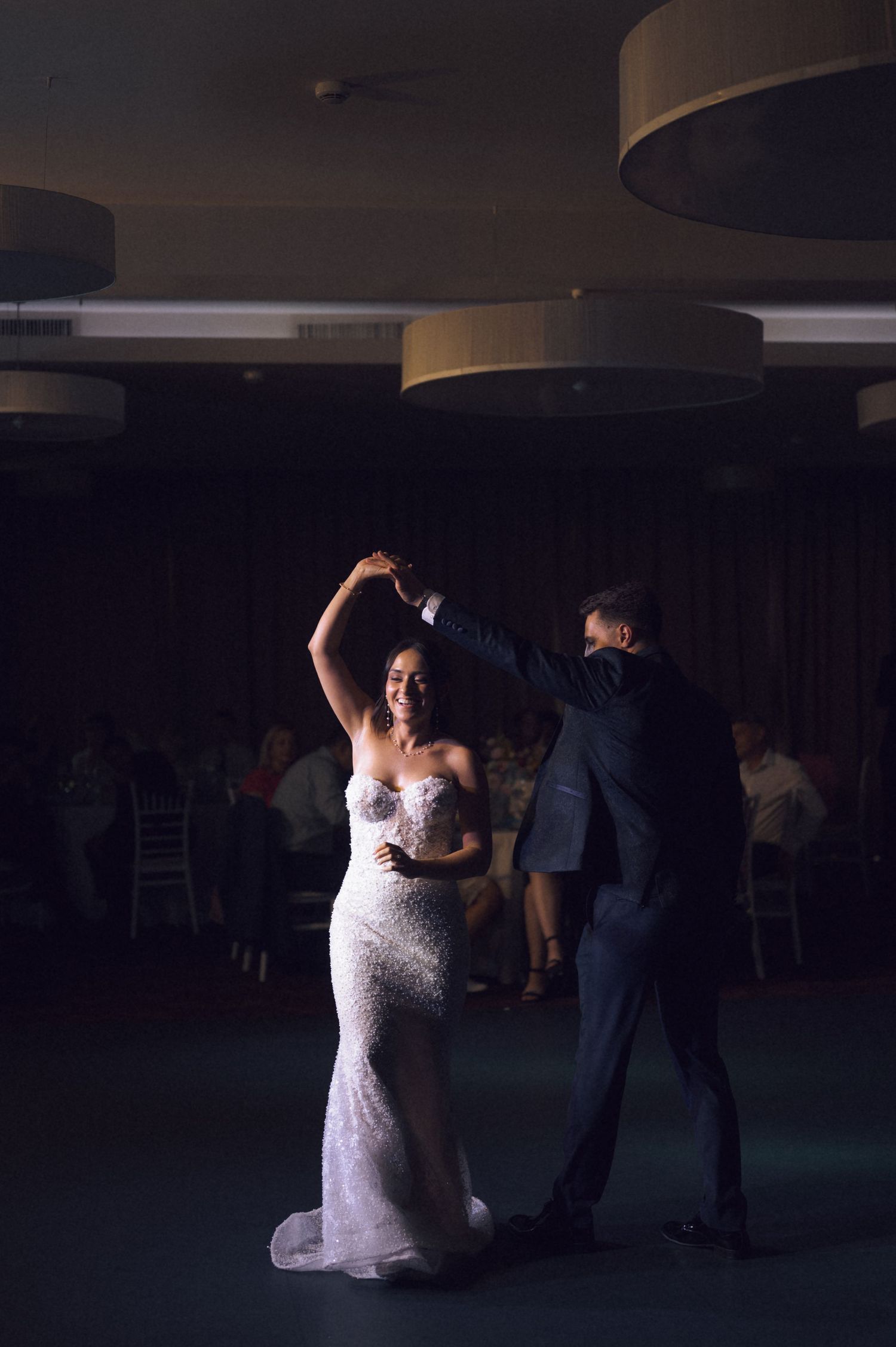 Bride in white gown spins on dance floor with groom in dark suit during elegant wedding reception.