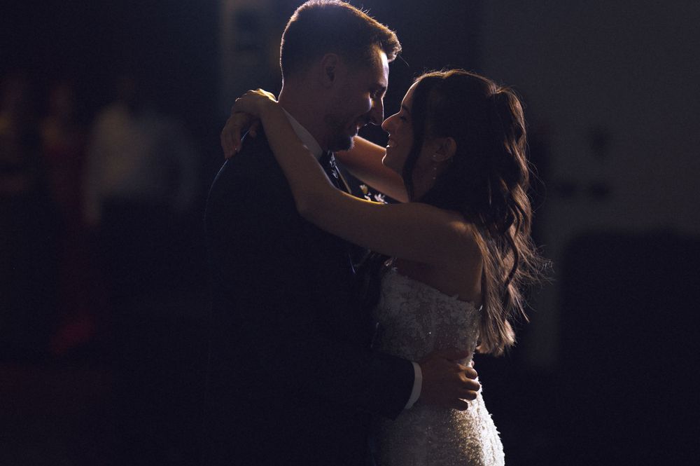 A bride and groom share an intimate first dance in soft dramatic lighting at their wedding reception.