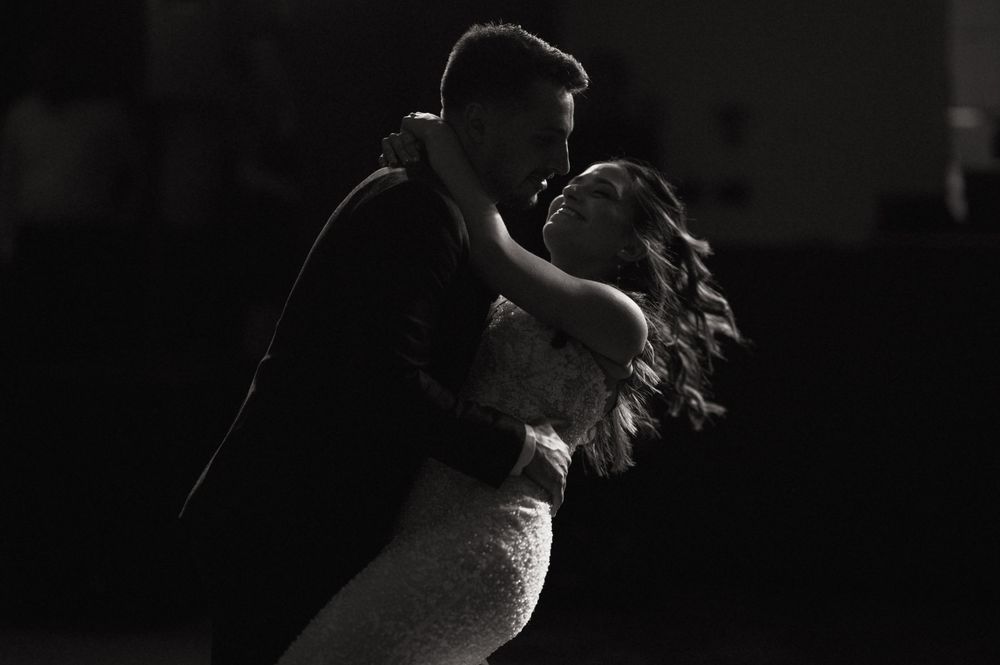 Black and white photo of a couple sharing a romantic dip dance, bride in lace gown, groom in dark suit.