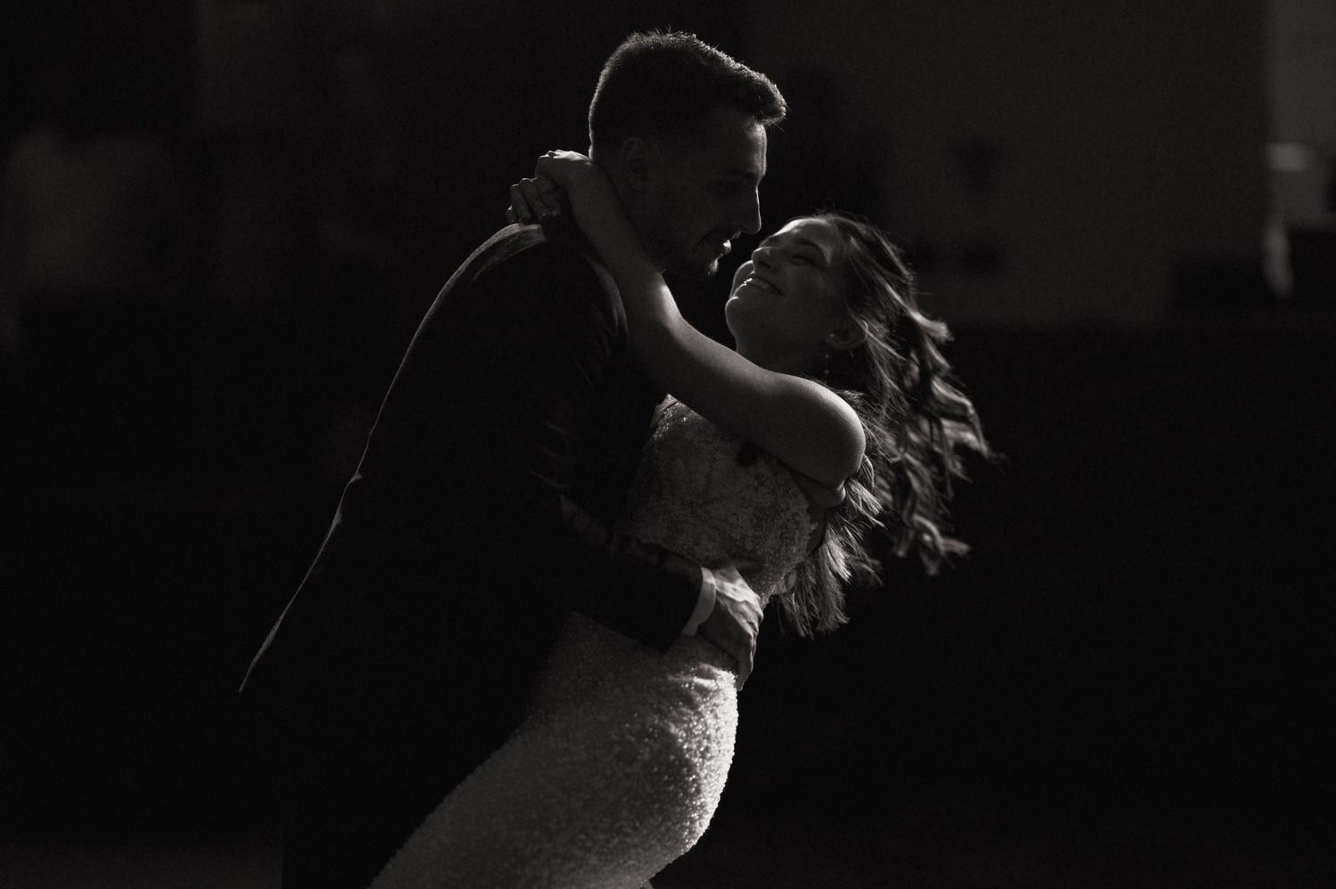 Black and white photo of a couple sharing a romantic dip dance, bride in lace gown, groom in dark suit.