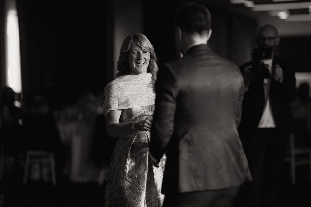 Black and white photo of a woman in a sequined dress laughing joyfully with a man in a suit at a wedding reception.