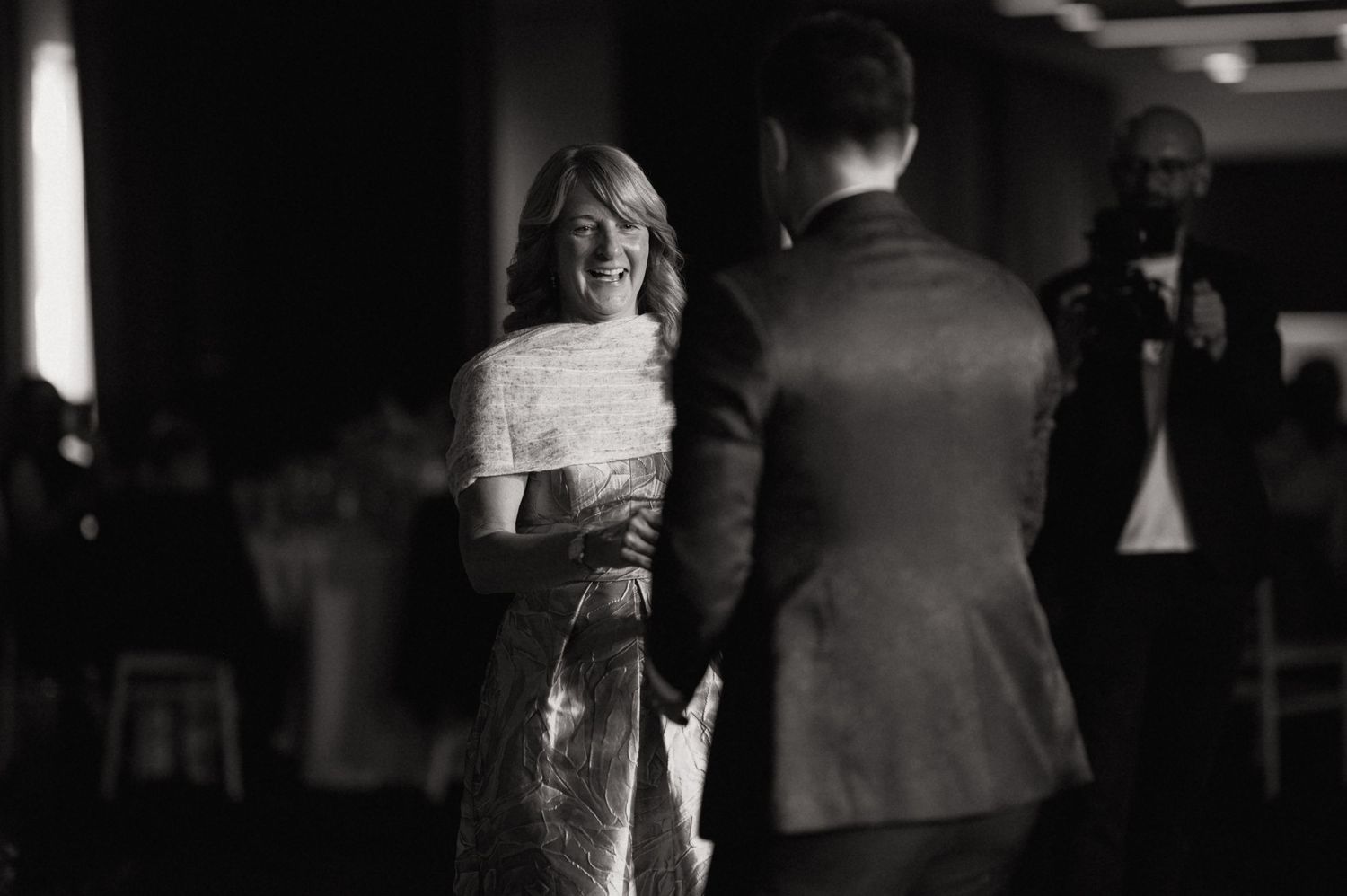 Black and white photo of a woman in a sequined dress laughing joyfully with a man in a suit at a wedding reception.