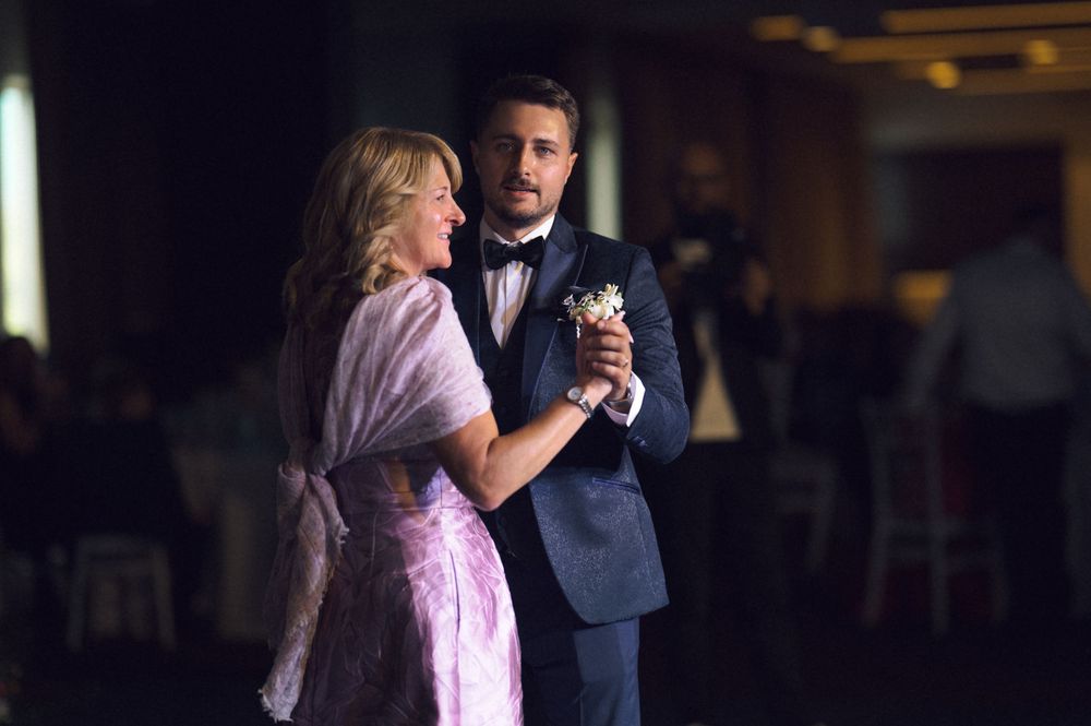 A man in a navy suit and woman in pink dress share a romantic dance at an elegant evening reception.
