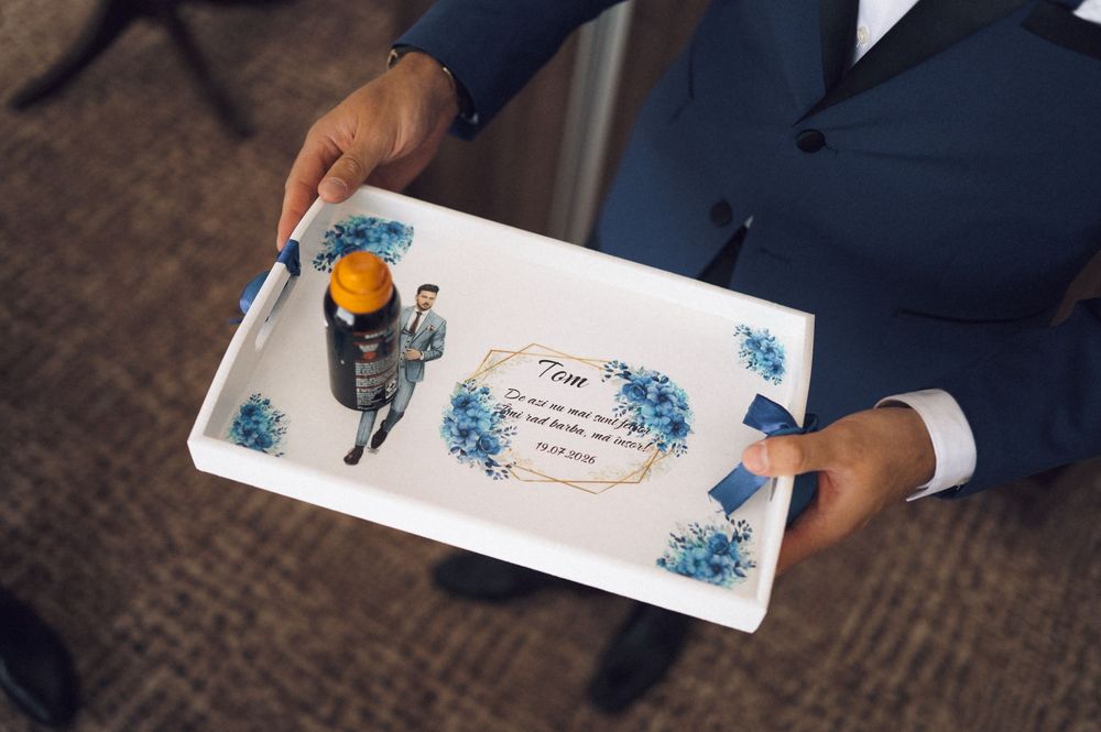 Man in blue suit holding a personalized white decorative tray with blue floral design and a bottle.