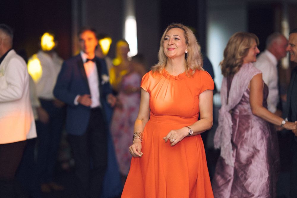 Woman in elegant orange dress smiling at a formal event with guests in background.