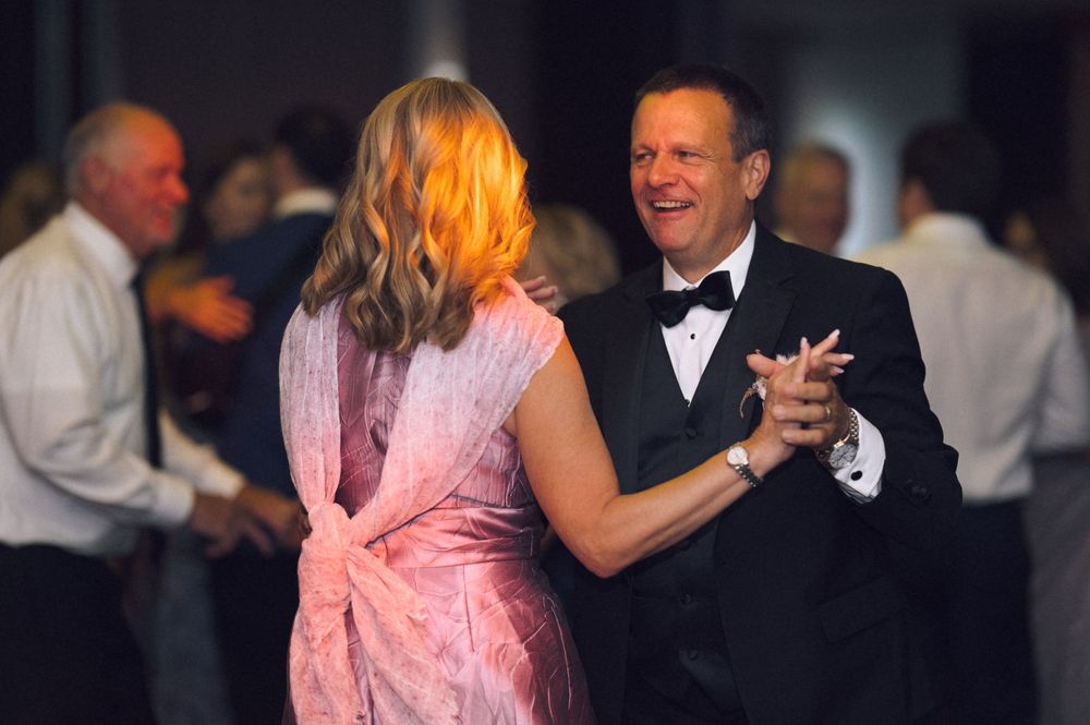 Elegant couple dancing at formal gala event, man in tuxedo and woman in pink dress, surrounded by guests.