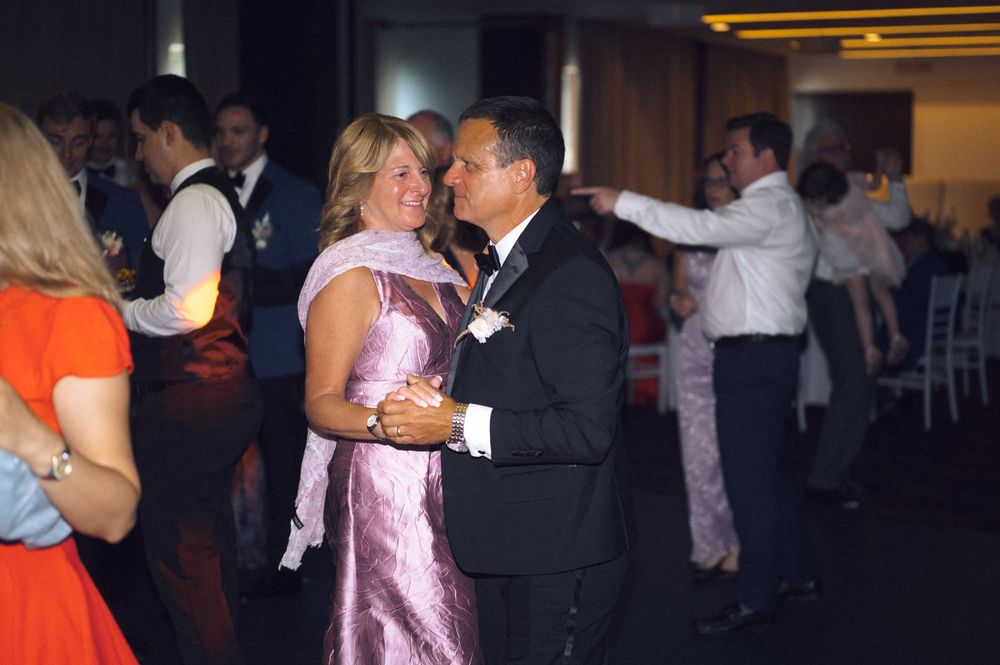 Couple dancing elegantly at a formal event, woman in pink gown, man in black suit, guests dancing in background.