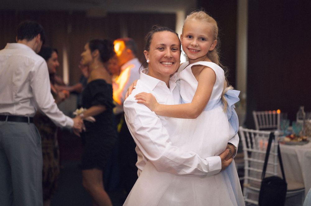 Woman in white dress holding young blonde girl in flower girl dress at a wedding reception dance floor.