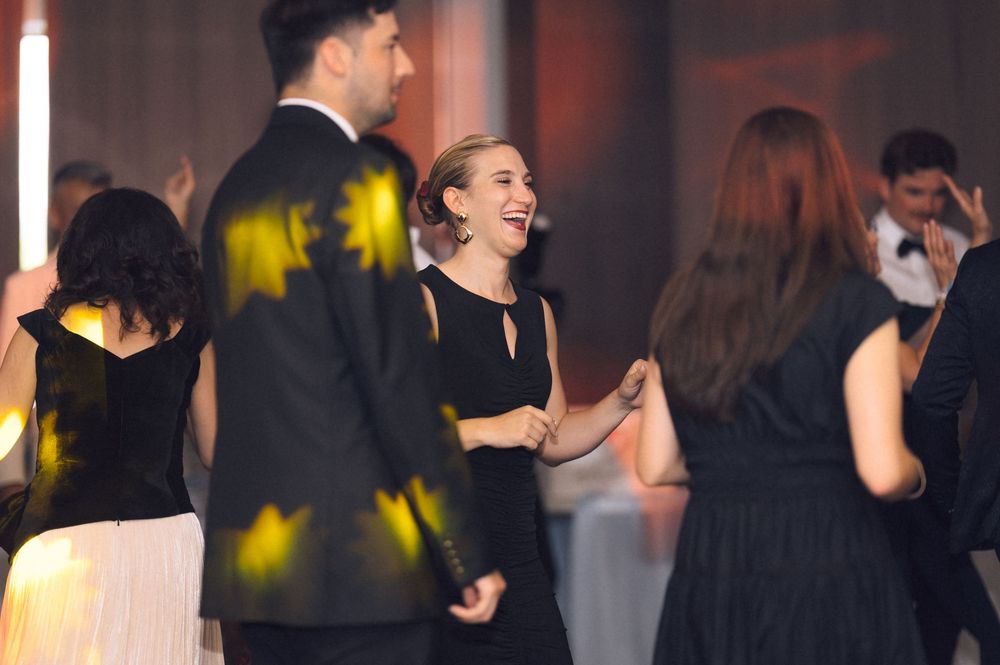 Elegantly dressed guests in black tie attire laughing and socializing at a formal evening gala event.