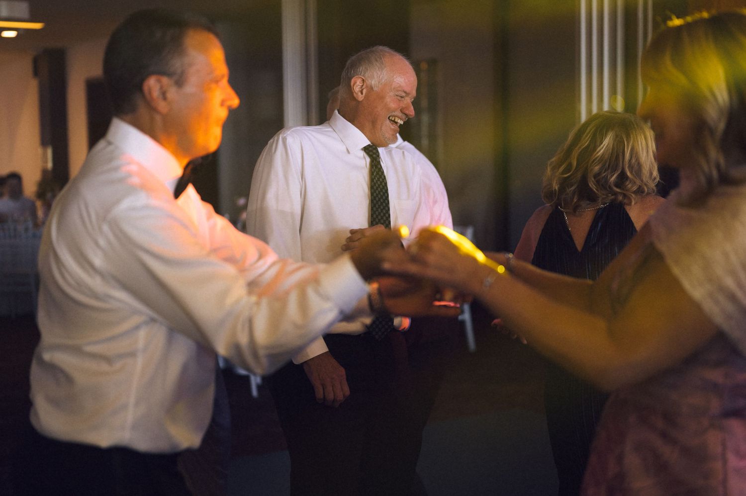 People dancing and socializing at an indoor evening event, men in dress shirts and ties enjoying a festive celebration.