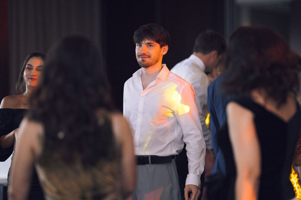Young man in white shirt standing among guests at a formal evening event or gala.