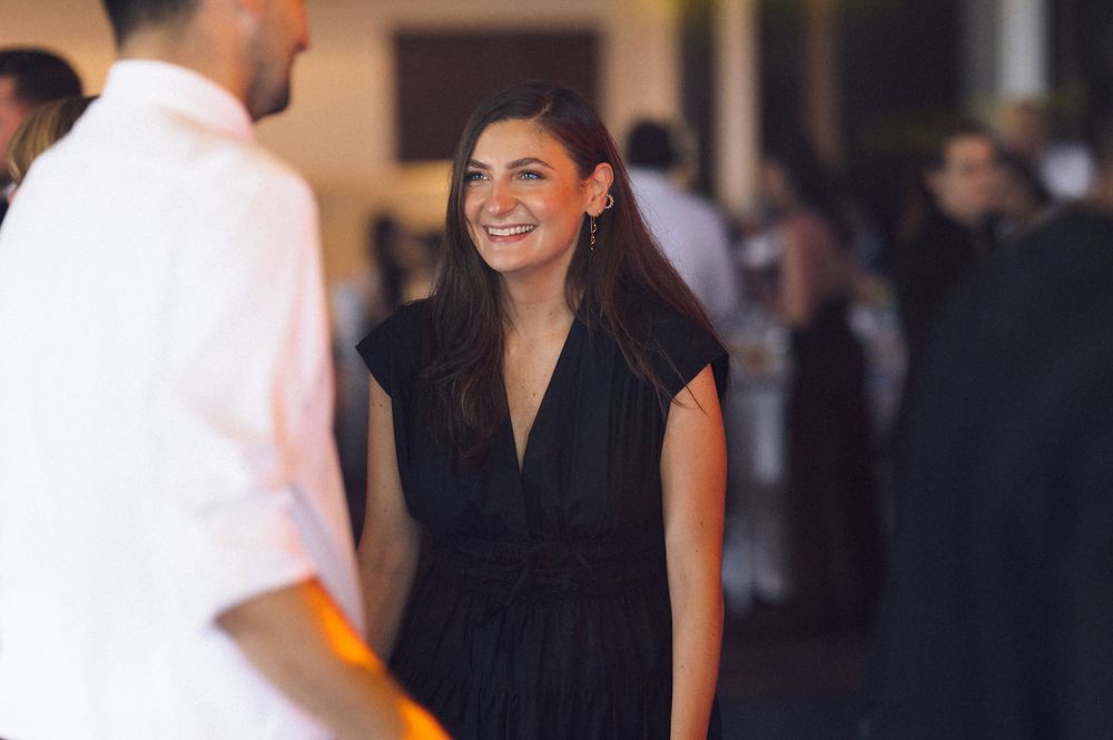Woman in black dress smiling at a social event, engaged in conversation at an elegant gathering.