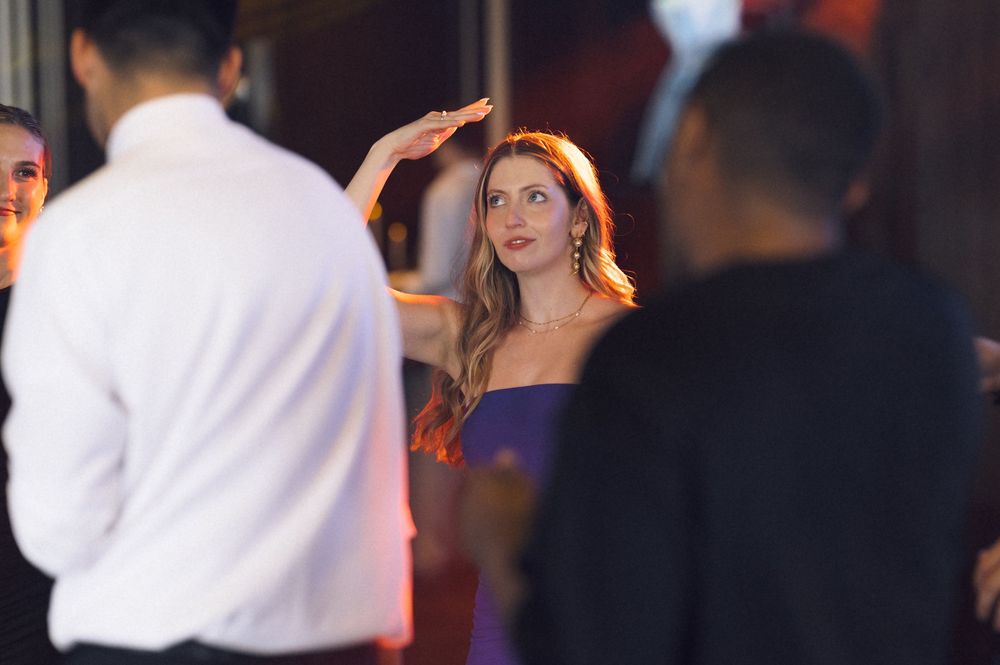 Elegant woman in purple dress at upscale event, surrounded by guests in formal attire under warm lighting.