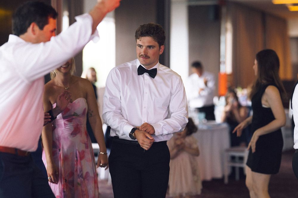 Man in white dress shirt and black bow tie stands at a formal wedding reception event.