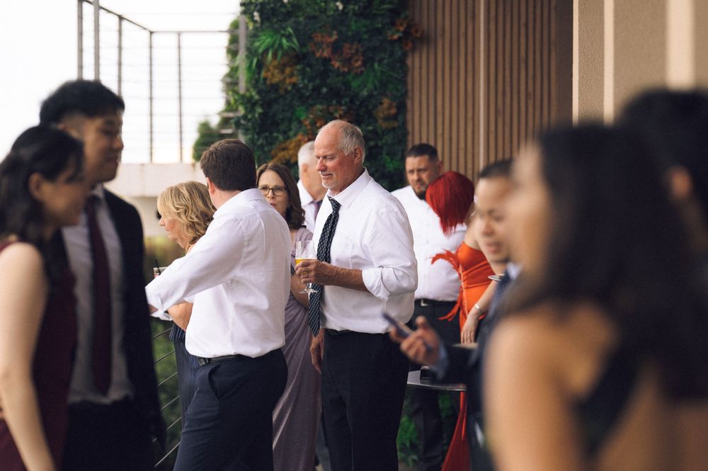 Guests mingling at an elegant outdoor wedding reception, dressed in formal attire on a stylish venue terrace.