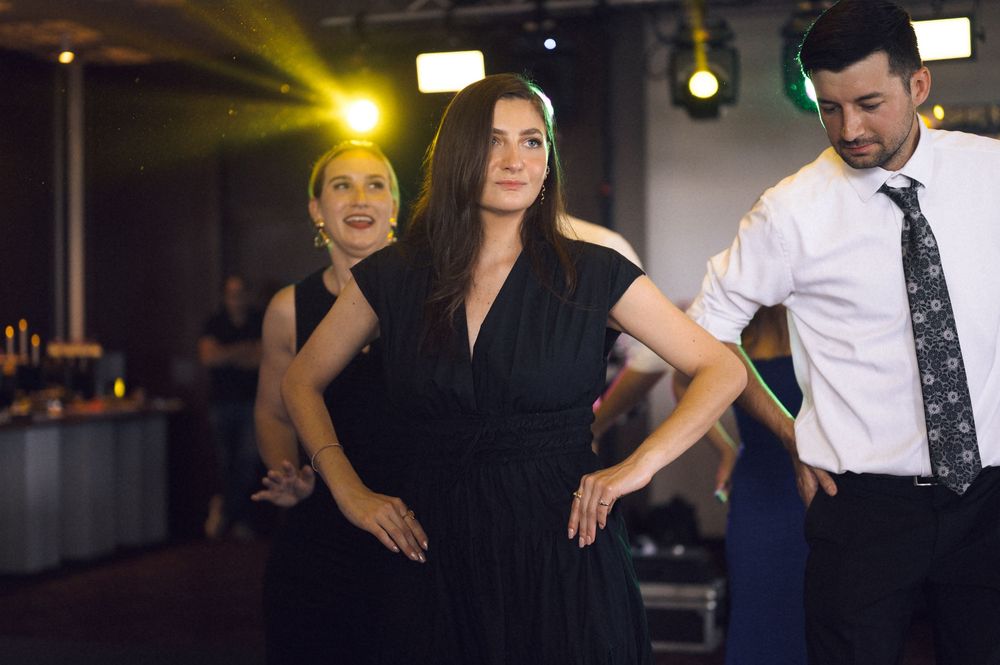 Three elegantly dressed people dancing at a formal event, woman in black dress with hands on hips.
